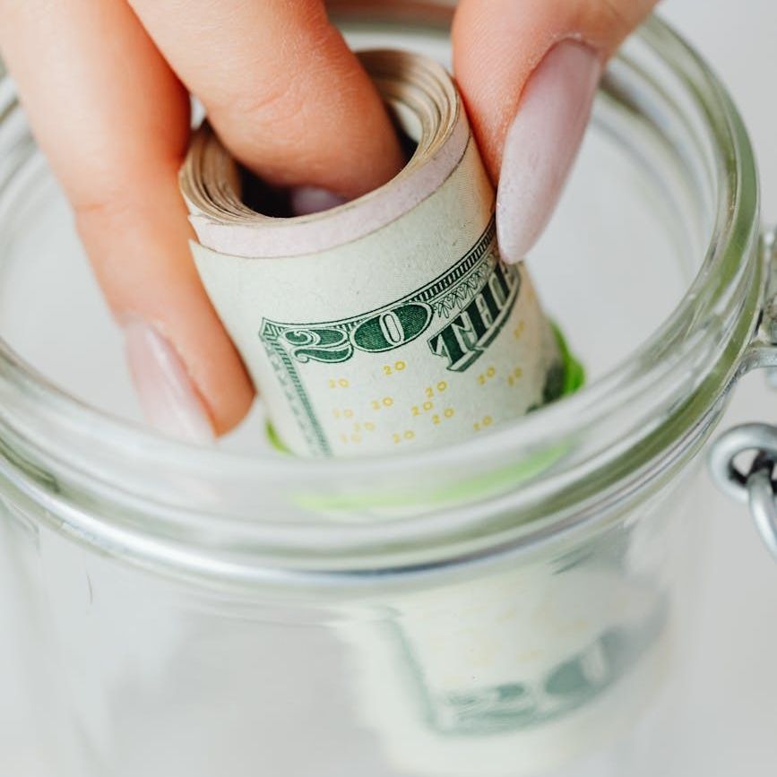 Rolled money being put inside a glass jar. 