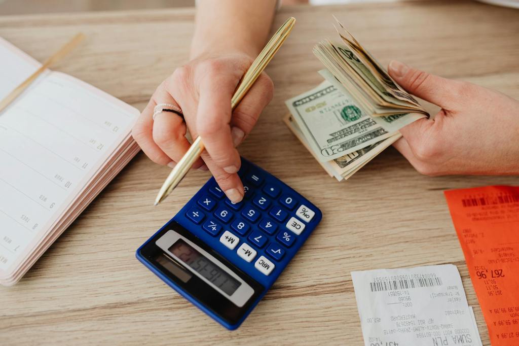 A person uses a calculator, pen, receipts, and a calender while holding money.